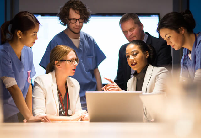 a group of healthcare professionals gather around a laptop