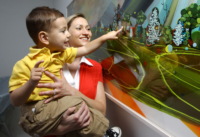 a woman holds up a small boy to touch a painting
